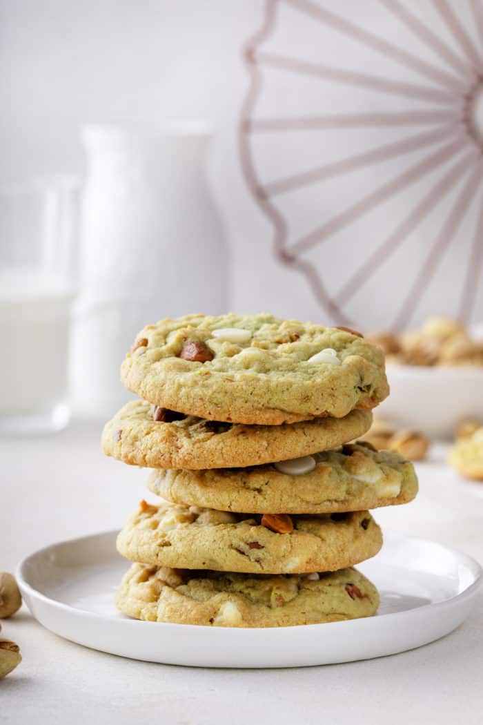 5 white chocolate pistachio pudding cookies stacked on a white plate.