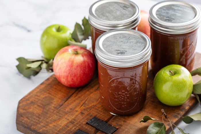 Three jars of canned apple butter on a wooden board.