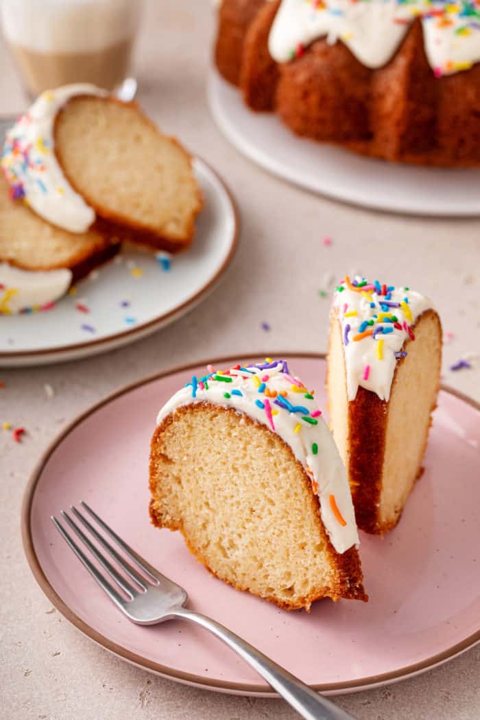 Two slices of easy vanilla bundt cake sitting up on a pink plate.
