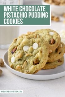 Three white chocolate pistachio pudding cookies stacked on a white plate. A fourth cookie is leaning against the stack. text overlay includes recipe name.