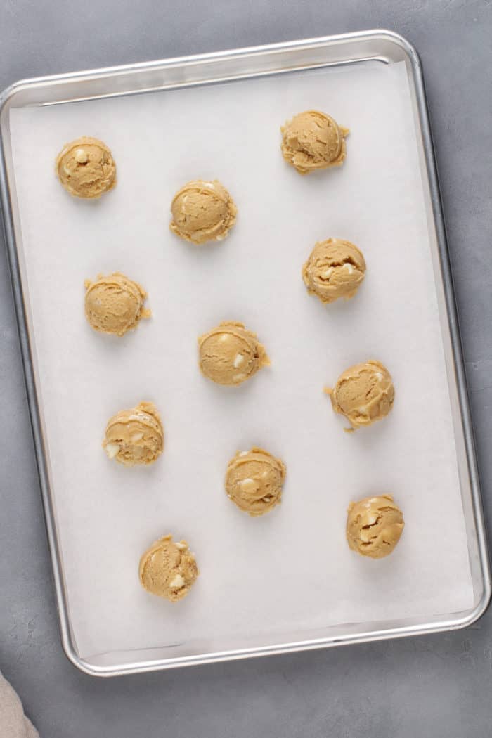 White chocolate macadamia nut dough balls on a parchment-lined baking sheet.