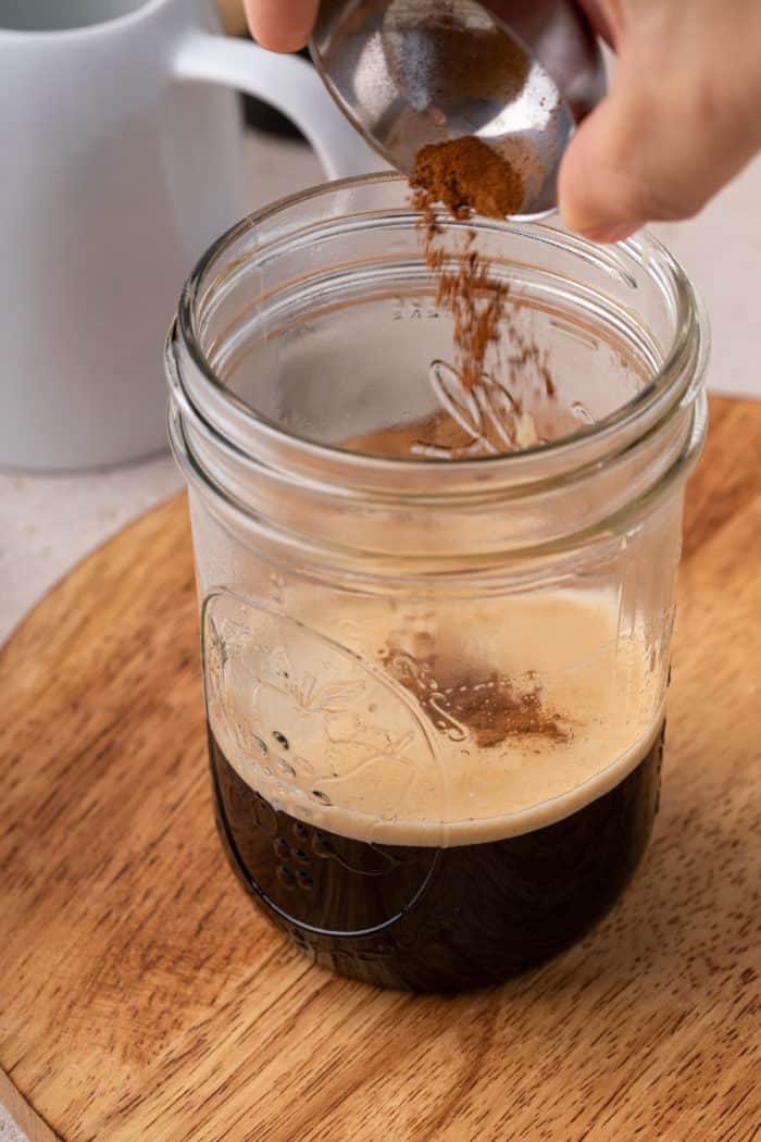 Adding cinnamon to espresso in a mason jar.