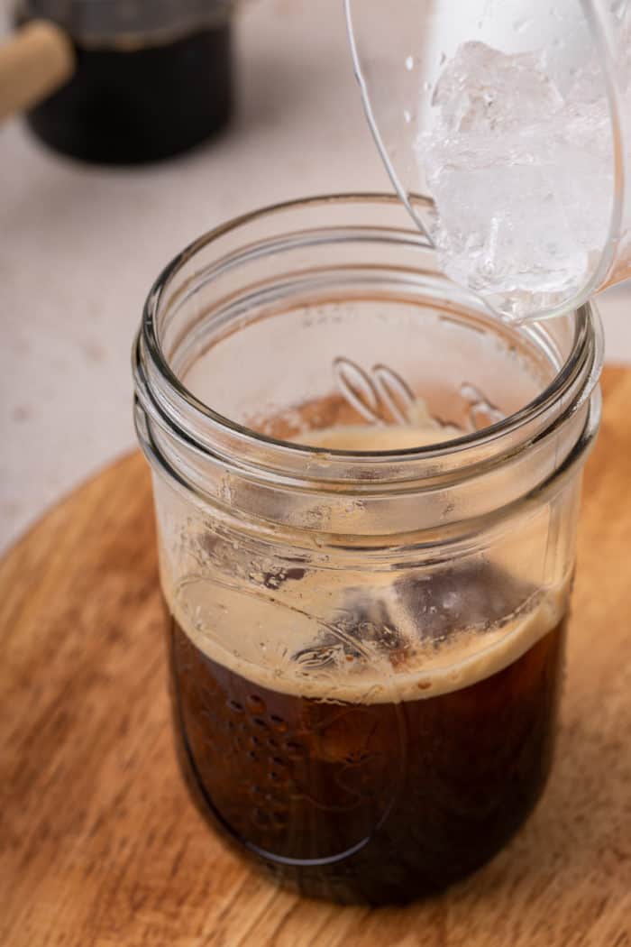 Adding ice to espresso in a mason jar.