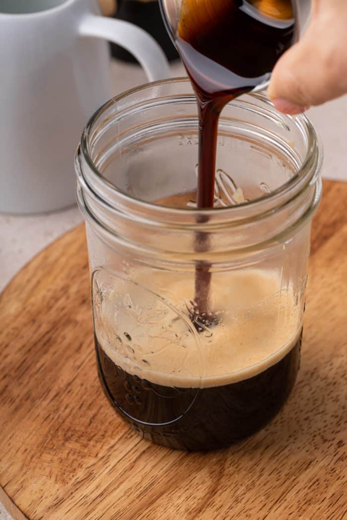 Pouring brown sugar syrup into espresso in a mason jar.