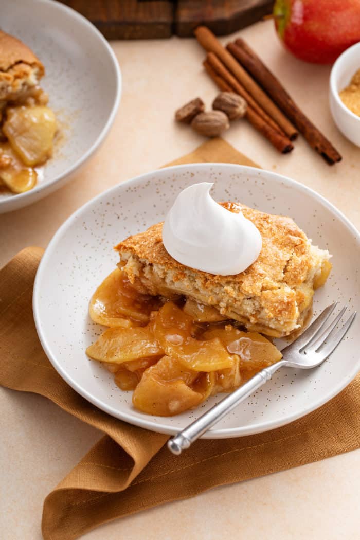 White bowl with a helping of apple cobbler topped with a dollop of whipped cream.