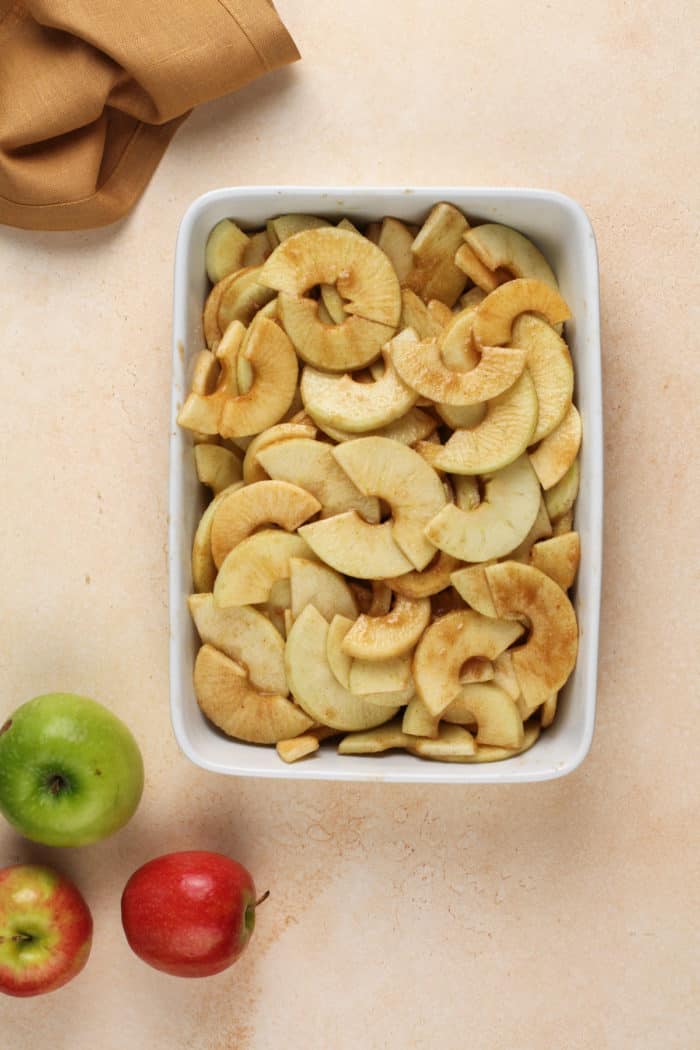 Apples tossed with sugar and spices in a white baking dish.