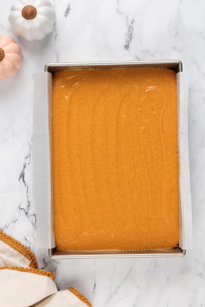 Assembled pumpkin gooey butter cake in a parchment-lined pan, ready to go in the oven.