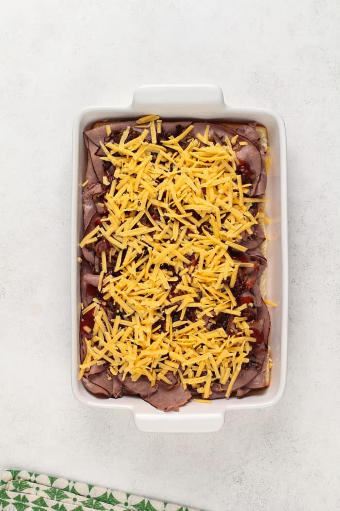 Assembled cheesy roast beef sliders in a white baking dish.