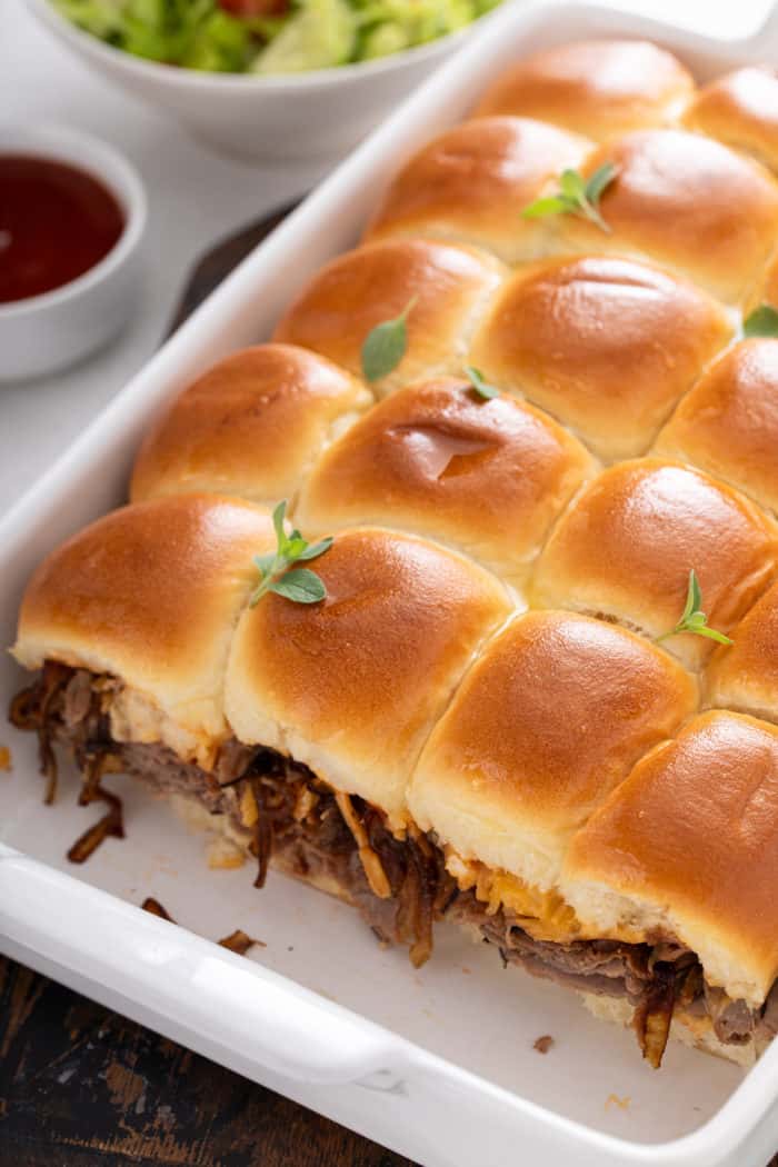 Baked cheesy roast beef sliders in a white pan.