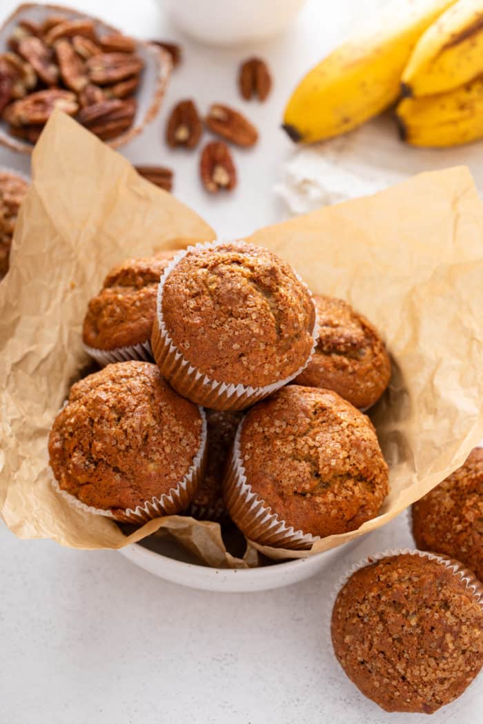 Five banana nut muffins arranged in a parchment-lined white bowl.