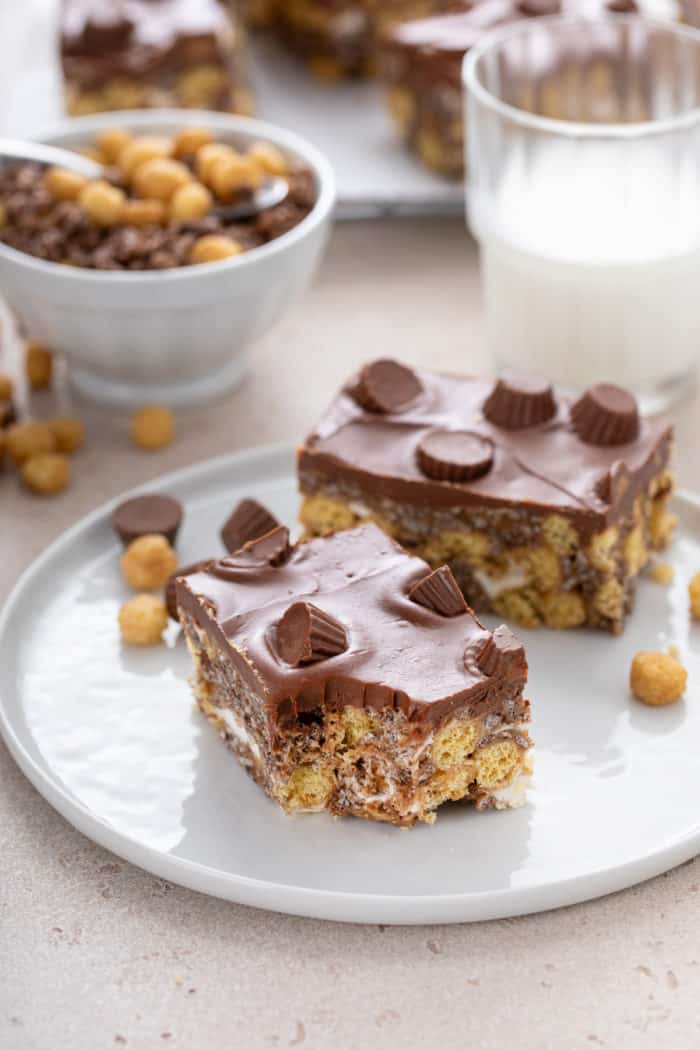 Two peanut butter cup rice krispie treats on a plate. A bite has been taken from the corner of the treat closest to the camera.