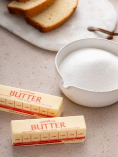 Bowl of sugar and two sticks of butter on a beige countertop.