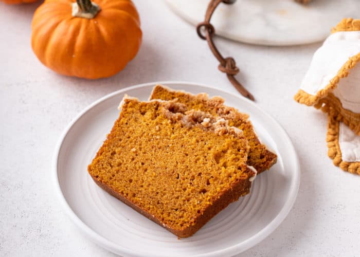 White plate holding two slices of streusel-topped pumpkin bread with maple glaze.