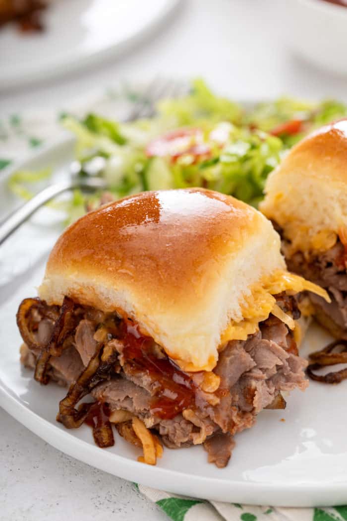 Close up of cheesy roast beef slider on a white plate.