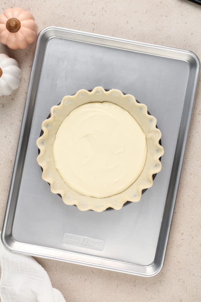 Cream cheese layer spread into the bottom of a crumped pie crust. The pie plate is set on a rimmed baking sheet.