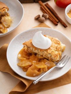 White bowl with a helping of apple cobbler topped with a dollop of whipped cream.
