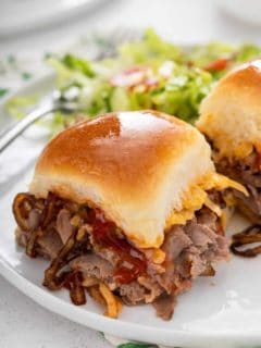 Close up of cheesy roast beef slider on a white plate.