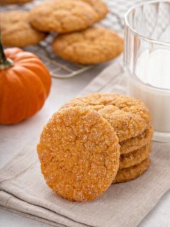 Four pumpkin snickerdoodles stacked on a cloth napkin with a fifth cookie leaning against the stack.