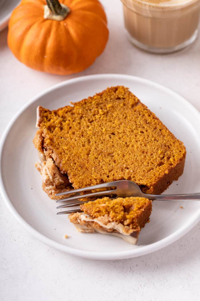 Fork cutting into a slice of streusel-topped pumpkin bread on a white plate.