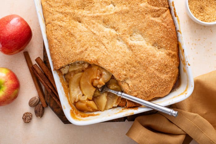 Overhead view of apple cobbler in a white baking dish with a serving taken from the corner.