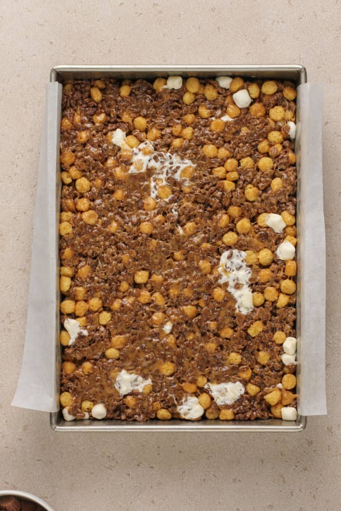 Base mixture for peanut butter cup rice krispie treats pressed into a parchment-lined pan.