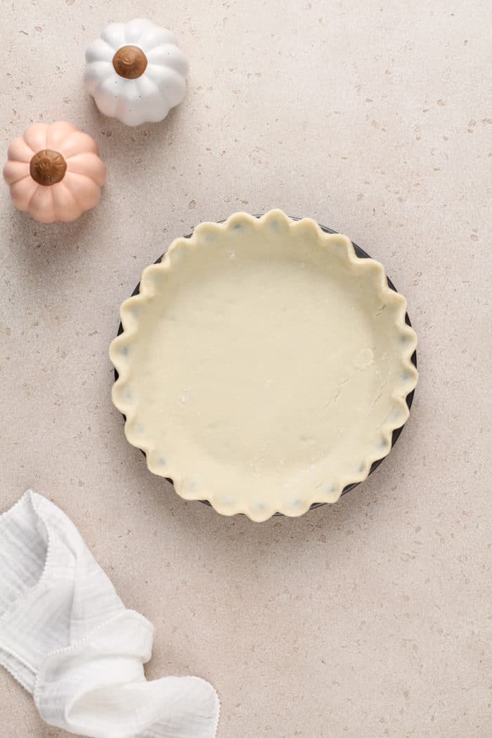 Crimped pie crust in a pie plate, set on a beige countertop.