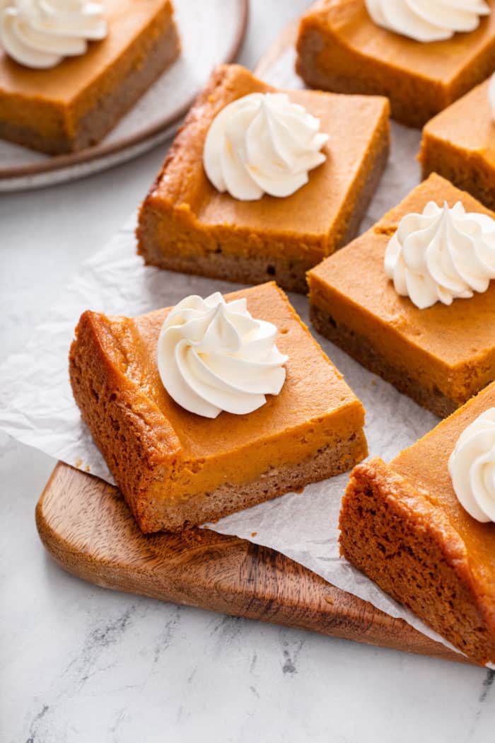 Several slices of pumpkin gooey butter cake arranged on a parchment-lined cutting board.