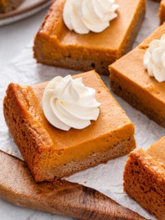 Slices of pumpkin gooey butter cake topped with whipped cream.
