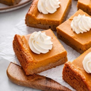 Slices of pumpkin gooey butter cake topped with whipped cream.