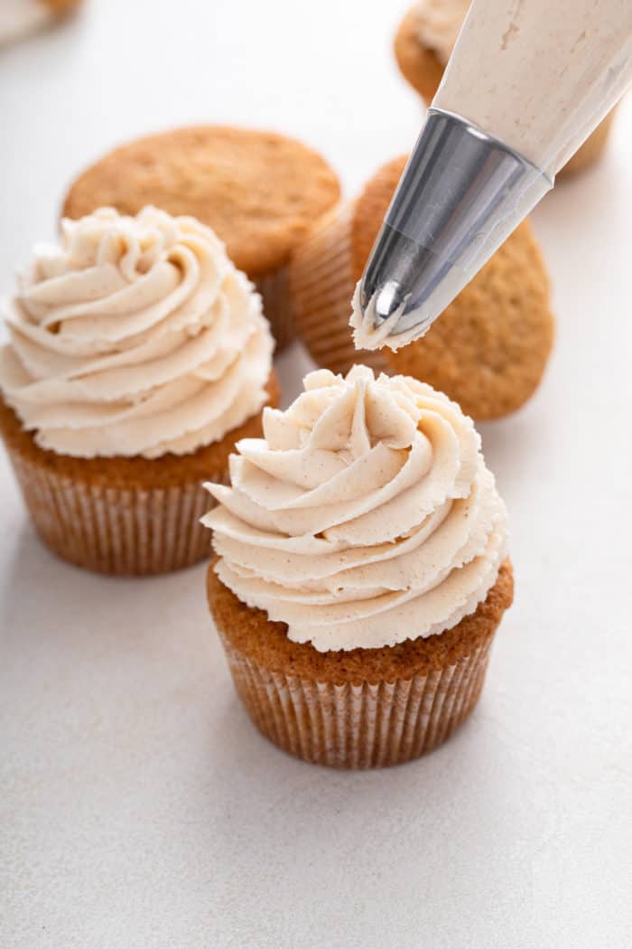 Piping bag finishing up piping brown butter frosting on a spice cupcake.