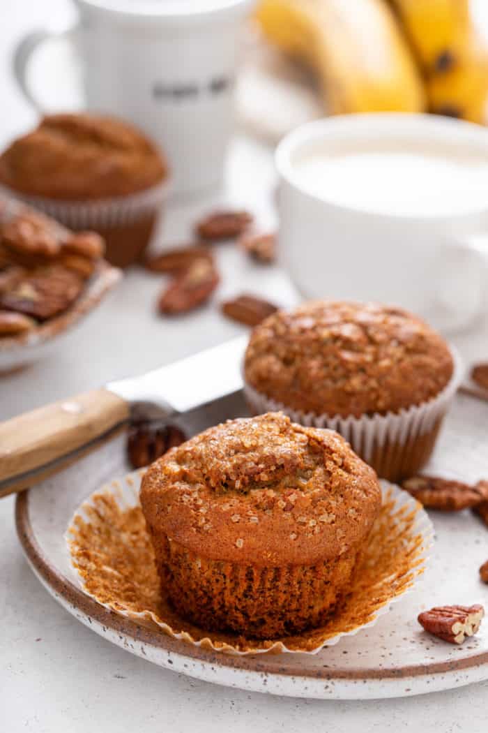 Two banana nut muffins on a plate. One muffin is unwrapped.