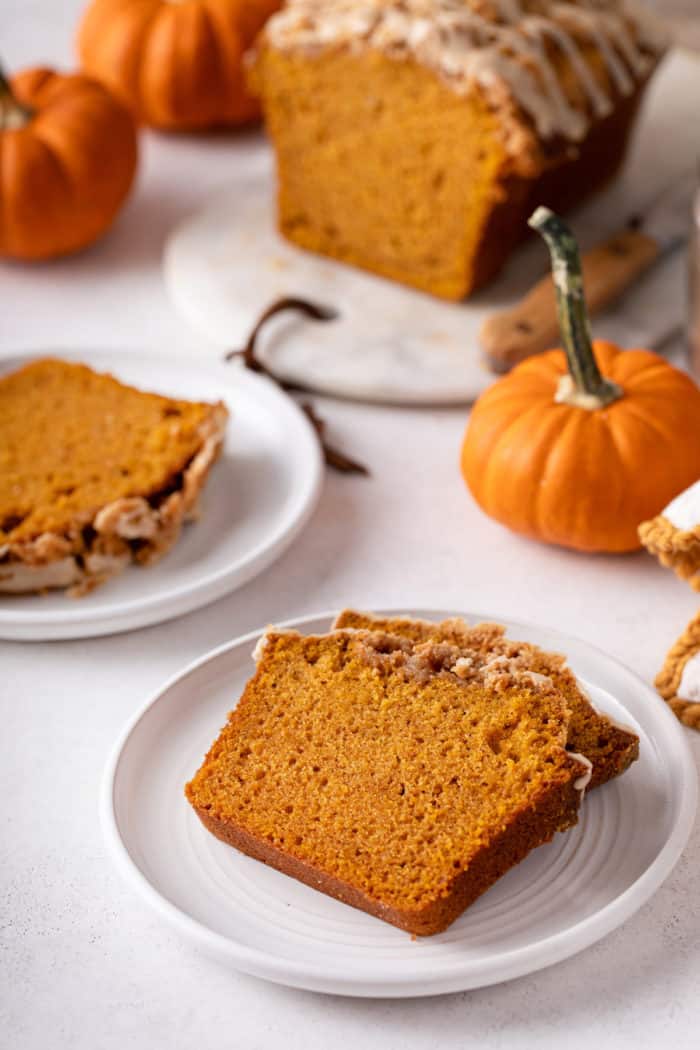 Two white plates, each holding slices of streusel-topped pumpkin bread with maple glaze.