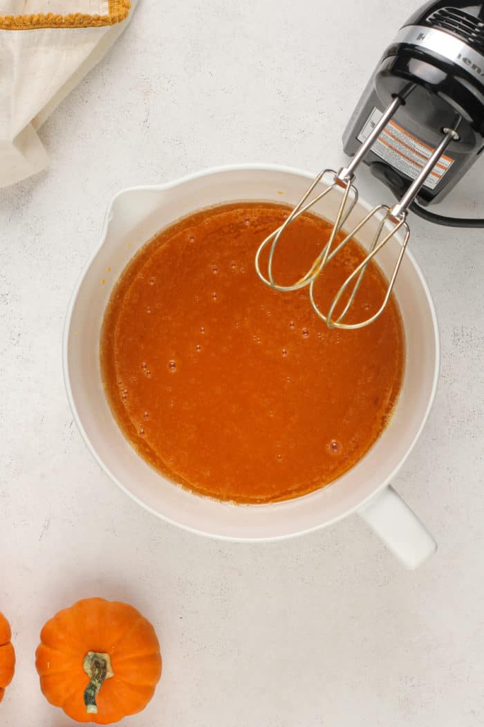 Wet ingredients for pumpkin bread in a white mixing bowl.