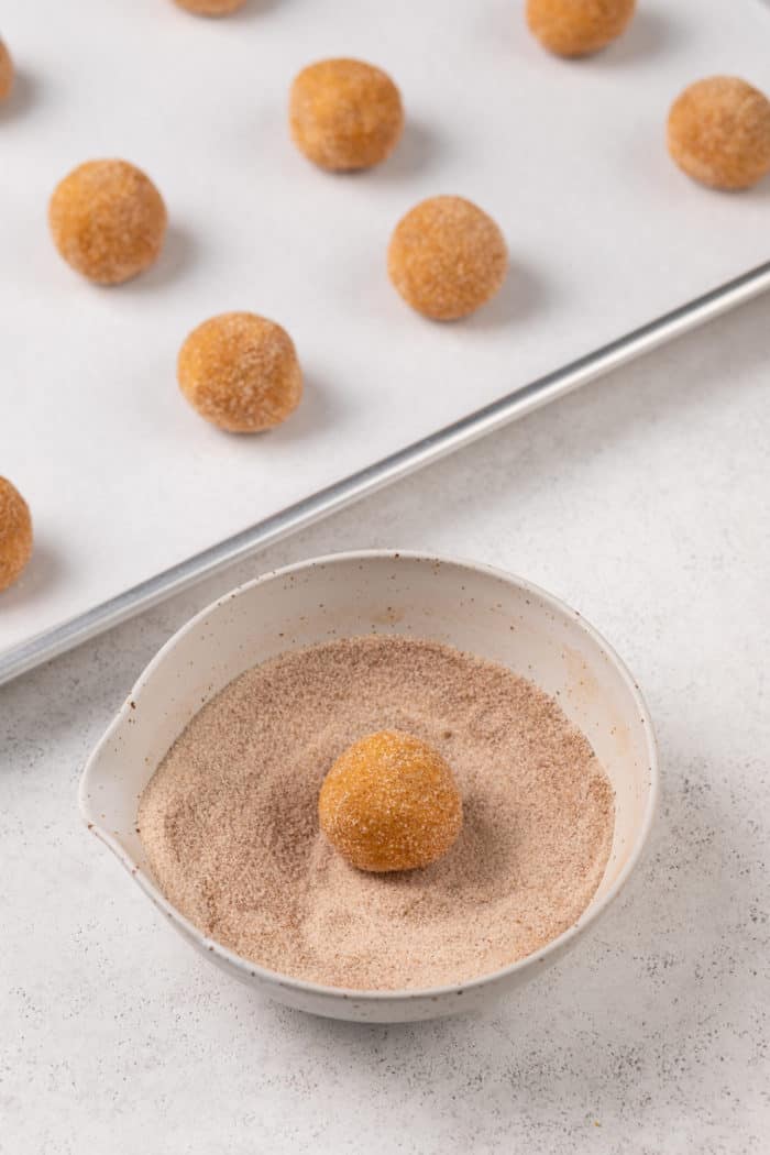 Dough ball being rolled in a spiced sugar mixture in a small bowl.