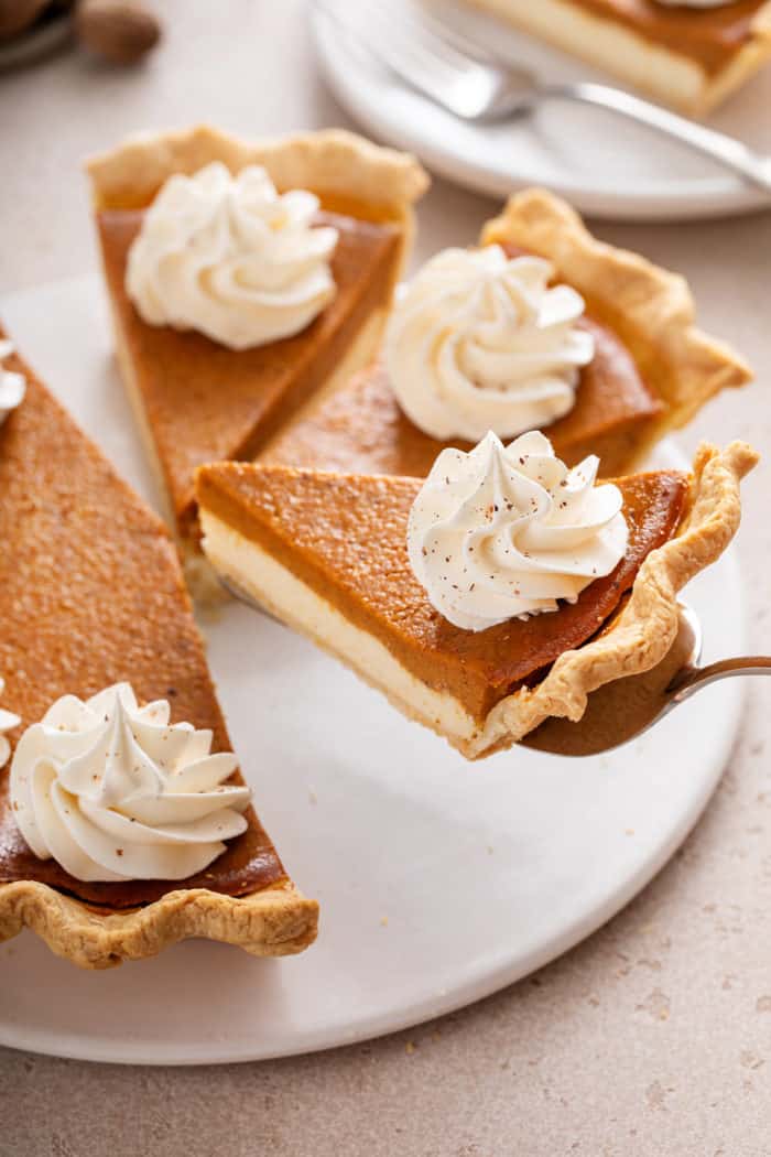 Pie server lifting up a slice of pumpkin cream cheese pie from a white platter.