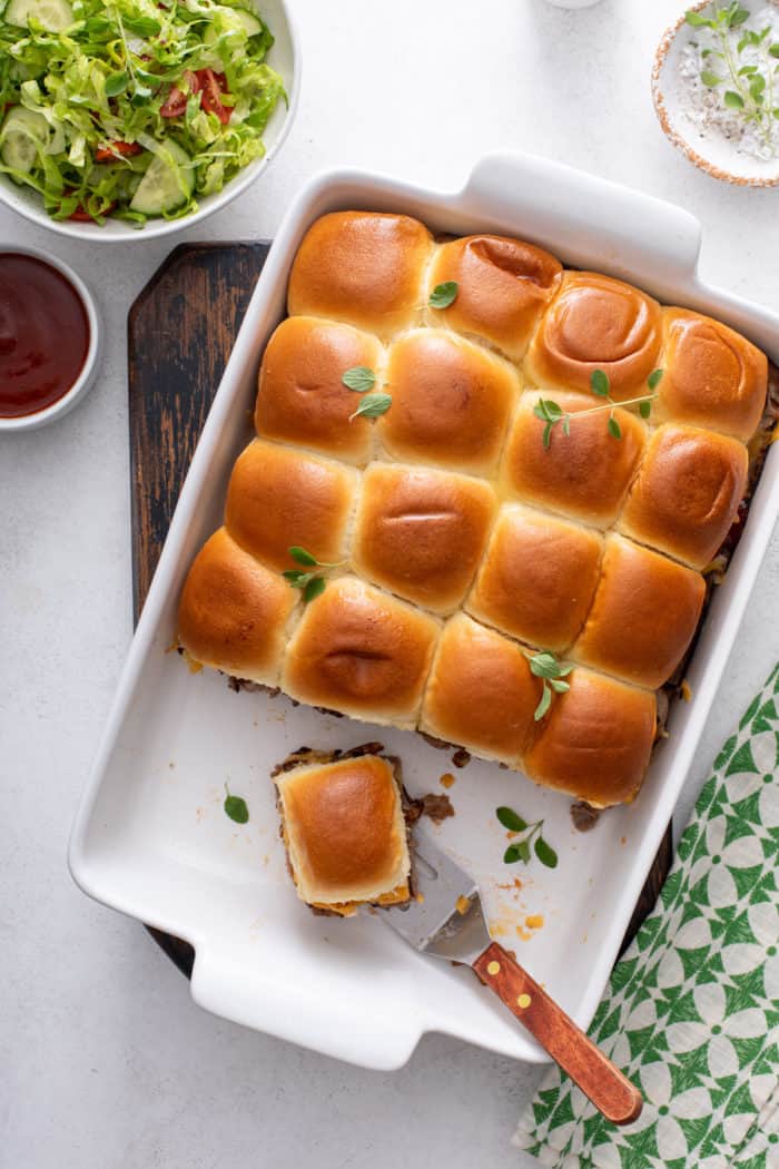 Metal server about to pick up a roast beef slider from a pan of sliders.