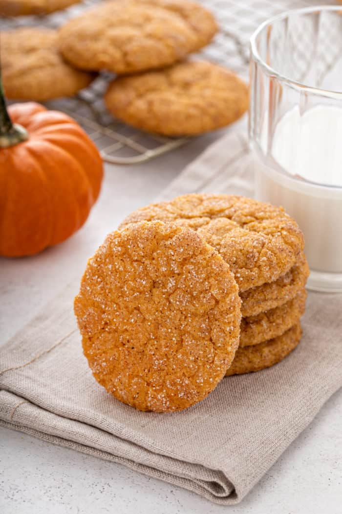 Four pumpkin snickerdoodles stacked on a cloth napkin with a fifth cookie leaning against the stack.