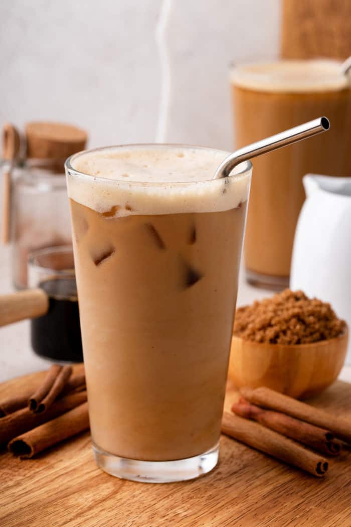 Tall glass filled with shaken espresso, set on a wooden board.