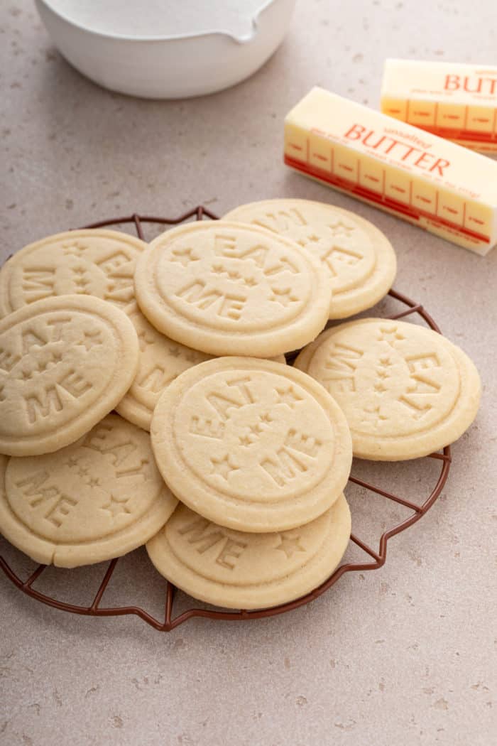 Stamped sugar cookies that each say "eat me" arranged on a metal rack.