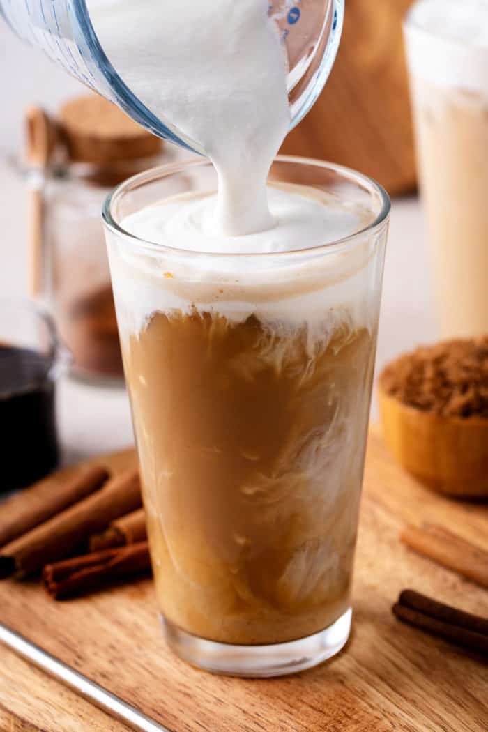 Vanilla sweet cream cold foam being poured over the top of a glass of iced coffee.