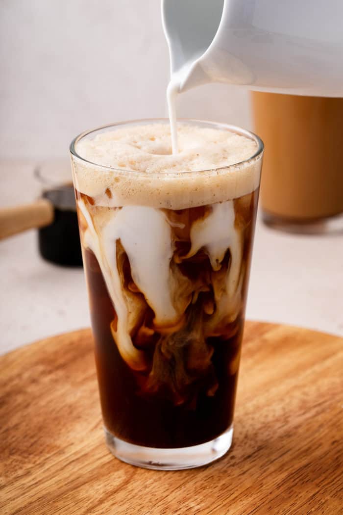 Milk being poured into a glass of iced shaken espresso.