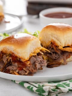 Two cheesy roast beef sliders on a white plate.