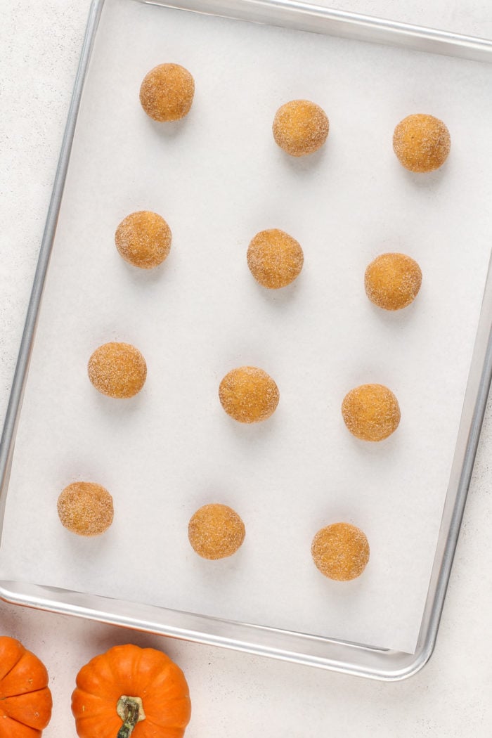 Balls of pumpkin snickerdoodle dough lined up on a baking sheet, ready to go in the oven.