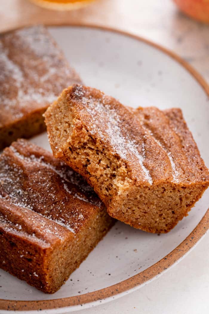 Apple cider blondie with a bite taken from the corner set against another blondie on a plate.