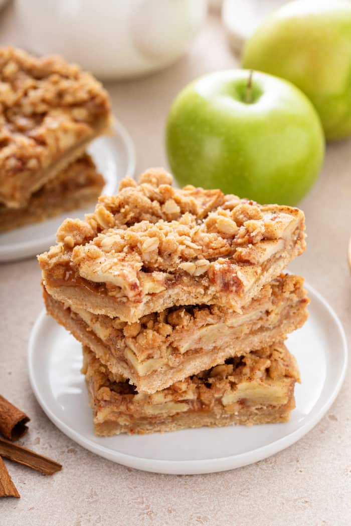 Three apple crisp bars stacked on a white plate. The top bar has a bite taken from the corner.