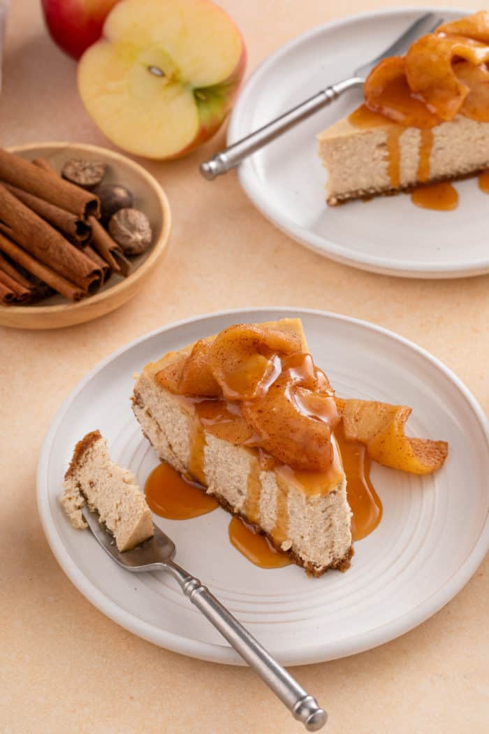 Slice of caramel apple cheesecake with a bite taken from the front on a plate next to a fork with the bite of cheesecake on it.