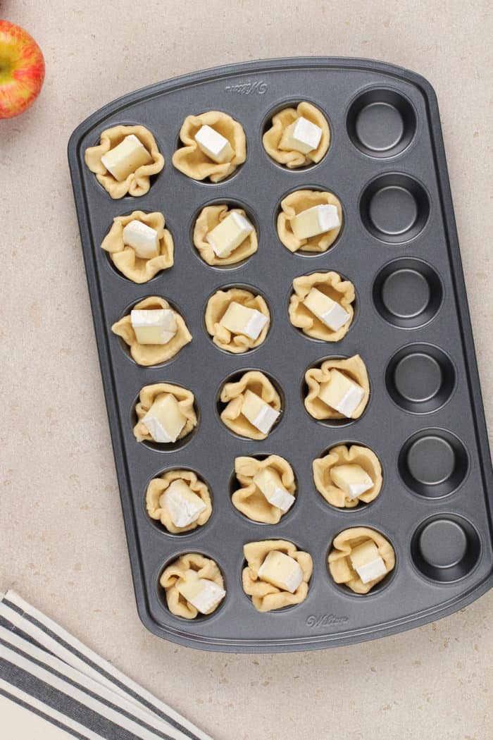 Pieces of brie in crescent roll cups in a mini muffin pan.