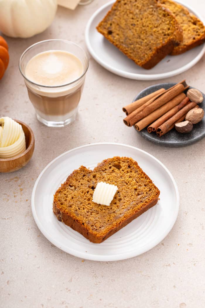 Slice of pumpkin banana bread on a white plate with a pat of butter on the top.