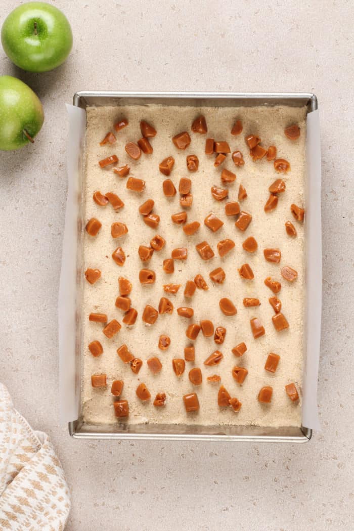 Caramel pieces scattered on the crust for apple crisp bars.