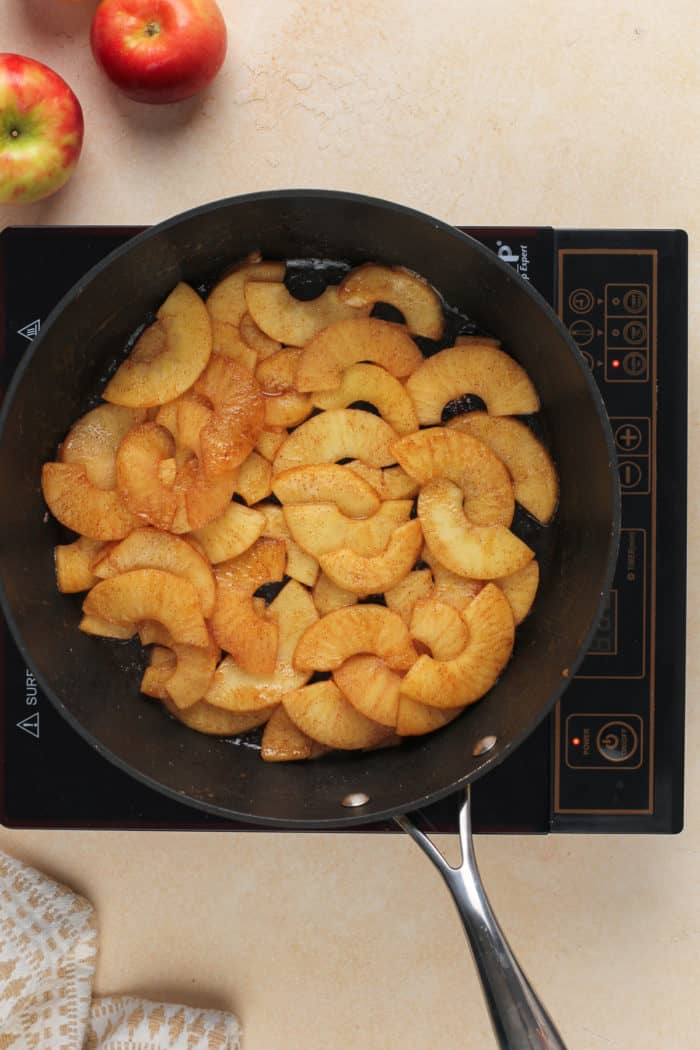 Cooked apples in a black skillet set on a burner.